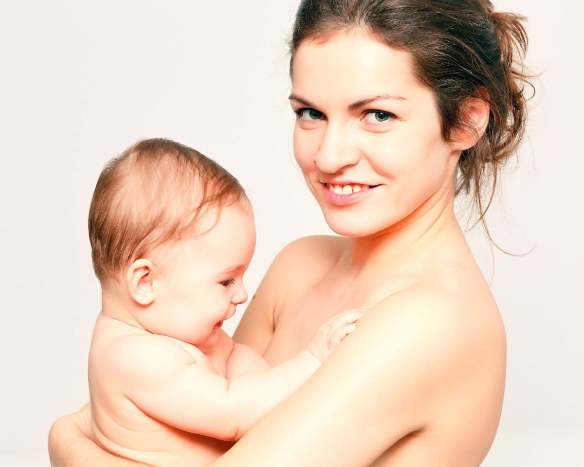 Mujer joven sosteniendo bebé después de tratamiento posparto para recuperar la elasticidad de la piel y tonificar los músculos