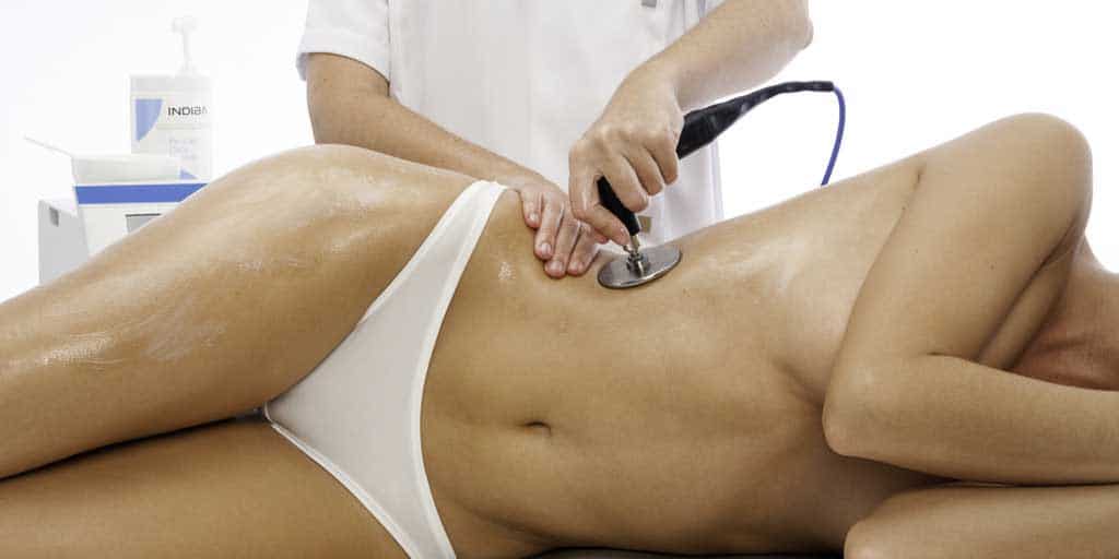 Mujer tumbada sobre camilla mientras médico usa aparatología de tratamiento para la menopausia