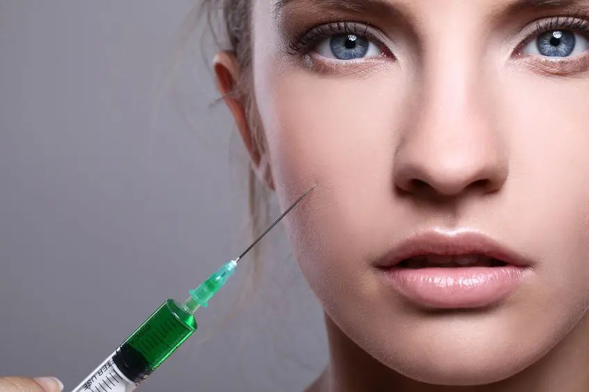 rostro de mujer joven recibiendo tratamiento de medicina estética mesoterapia facial con microinyecciones en la mejilla